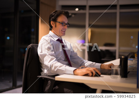 Happy Mature Businessman Sitting And Working In Office At Night Happy Mature Businessman Sitting And Working In Office At Night 59934825