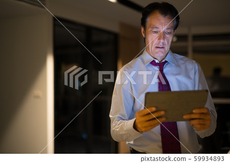 Mature Businessman In Office At Night Using Digital Tablet Computer Mature Businessman In Office At Night Using Digital Tablet Computer 59934893