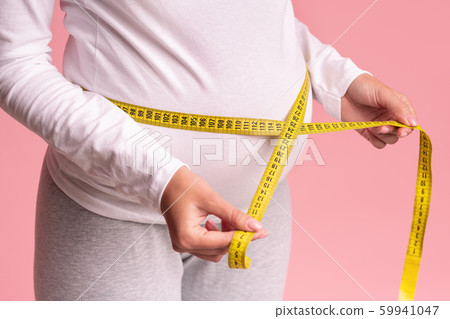 Unrecognizable Pregnant Lady Measuring Belly Standing Over Pink Background, Cropped Unrecognizable Pregnant Lady Measuring Belly Standing Over Pink Background, Cropped 59941047