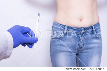 The doctor holds a scalpel on the background of the abdomen of the girl. The concept of surgery for inflammation of appendicitis, medical 59942844