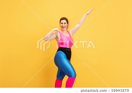 Young caucasian plus size female model's training on yellow background 59943879