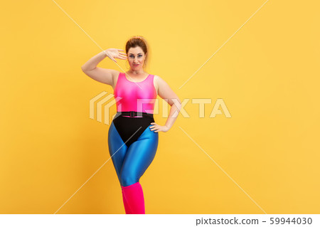 Young caucasian plus size female model's training on yellow background Young caucasian plus size female model's training on yellow background 59944030