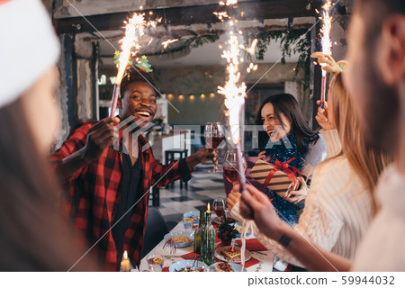 Friends having a party. Smiling people on a holiday toasting drinks burning sparklers Friends having a party. Smiling people on a holiday toasting drinks burning sparklers 59944032
