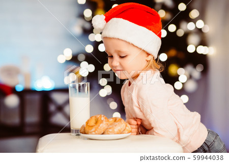 Cute little girl looking at treats for Santa near Christmas tree Cute little girl looking at treats for Santa near Christmas tree 59944038