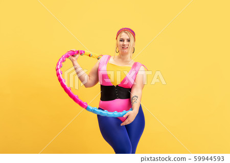Young caucasian plus size female model's training on yellow background Young caucasian plus size female model's training on yellow background 59944593