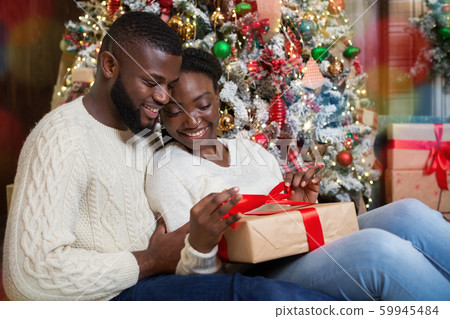 Happy afro woman opening Christmas gift from her caring husband 59945484