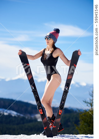 Sexy young woman holding skis in black swimsuit and sunglasses on background of mountain landscape. 59945546