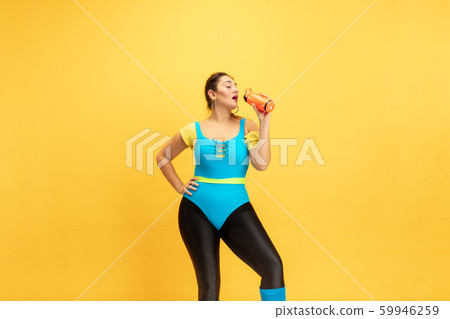 Young caucasian plus size female model's training on yellow background 59946259