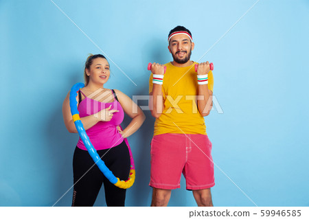 Young pretty caucasian couple in bright clothes training on blue background Young pretty caucasian couple in bright clothes training on blue background 59946585