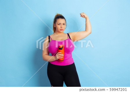 Young caucasian plus size female model's training on blue background 59947201