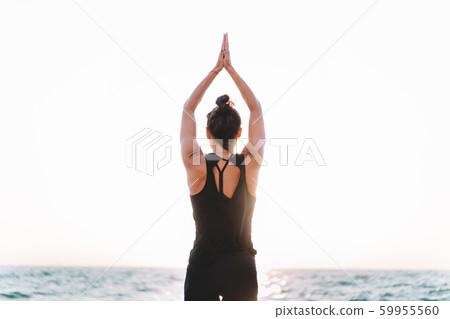 Slim woman in black bodysuit practicing yoga near sea or ocean during sunrise light. Flexibility, stretching, fitness, healthy lifestyle.  59955560