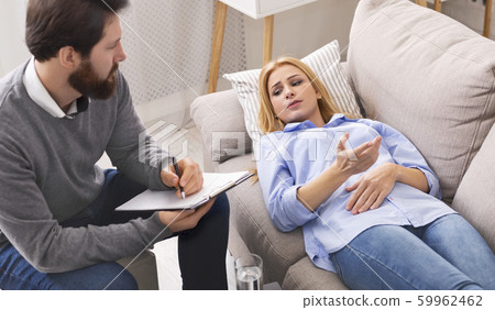 Stressed patient on sofa talking to psychologist at consultation