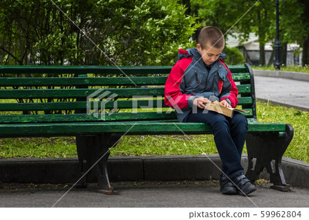 Horizontal image of boy reading a book on bench 59962804