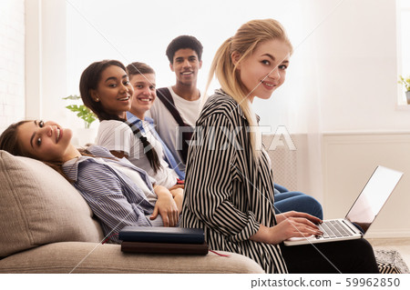 Happy classmates with books and laptop resting on sofa 59962850