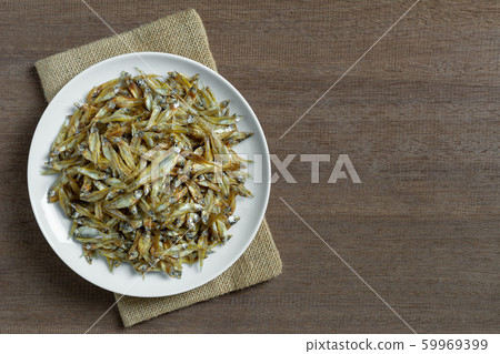 top view of roasted dried little fish with salt in a ceramic dish on wooden table. top view of roasted dried little fish with salt in a ceramic dish on wooden table. 59969399