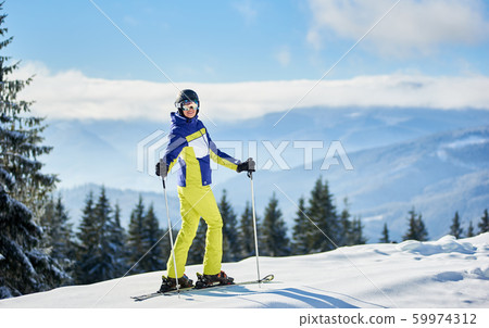 Happy woman skier posing on skis. Sunny day at ski resort. Panoramic view of mountain landscape on blurred background. 59974312