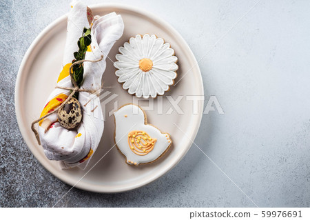 Table setting for the holiday of Easter. The photo shows white dishes, serving mat, Easter egg in a napkin. Napkin draped under rabbit ears. Table setting for the holiday of Easter. The photo shows white dishes, serving mat, Easter egg in a napkin. Napkin draped under rabbit ears. 59976691