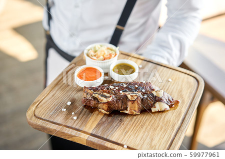 The waiter is holding a plate Beef meat cut according to the Argentine style, called asado. with 59977961