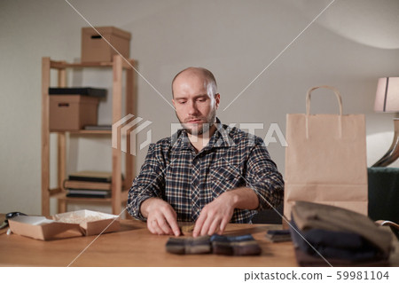 Man packs wool bow tie in box. Young man working as a tailor and using a sewing machine in workshop. 59981104