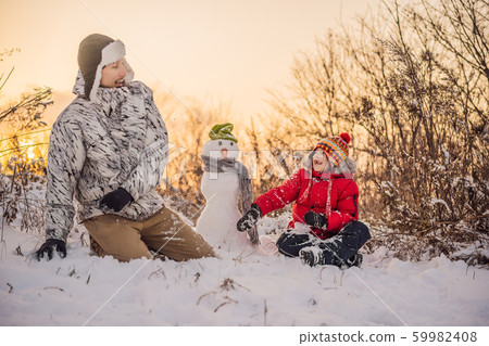 Happy family in warm clothing. Smiling Father and son making a snowman outdoor. The concept of Happy family in warm clothing. Smiling Father and son making a snowman outdoor. The concept of 59982408