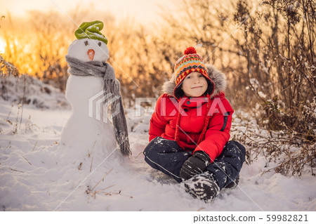 Cute boy in red winter clothes builds a snowman. Winter Fun Outdoor Concept Cute boy in red winter clothes builds a snowman. Winter Fun Outdoor Concept 59982821