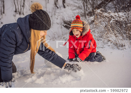 Happy family in warm clothing. Smiling mother and son making a snowman outdoor. The concept of Happy family in warm clothing. Smiling mother and son making a snowman outdoor. The concept of 59982972