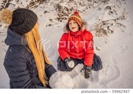 Happy family in warm clothing. Smiling mother and son making a snowman outdoor. The concept of Happy family in warm clothing. Smiling mother and son making a snowman outdoor. The concept of 59982987