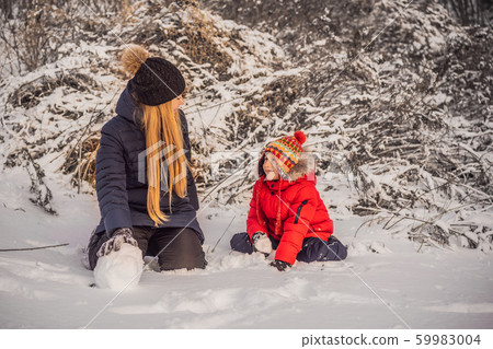 Happy family in warm clothing. Smiling mother and son making a snowman outdoor. The concept of Happy family in warm clothing. Smiling mother and son making a snowman outdoor. The concept of 59983004