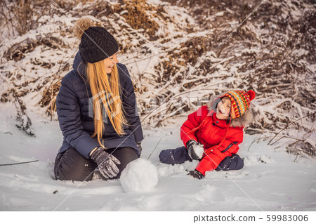 Happy family in warm clothing. Smiling mother and son making a snowman outdoor. The concept of Happy family in warm clothing. Smiling mother and son making a snowman outdoor. The concept of 59983006