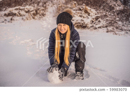 Young woman rolling giant snowball to make snowman 59983070