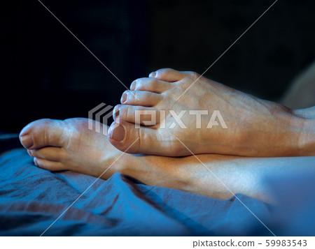 Female foot rise on the bed on a dark background Female foot rise on the bed on a dark background 59983543