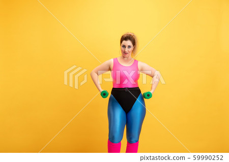 Young caucasian plus size female model's training on yellow background Young caucasian plus size female model's training on yellow background 59990252