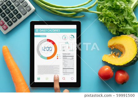 Calories counting , diet , food control and weight loss concept. woman using Calorie counter application on tablet at dining table with fresh vegetable and calculator Calories counting , diet , food control and weight loss concept. woman using Calorie counter application on tablet at dining table with fresh vegetable and calculator 59991500