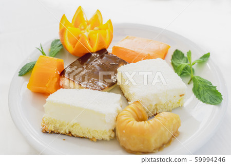 Oriental sweets decorated with orange on a white plate on a white background. Horizontal image Oriental sweets decorated with orange on a white plate on a white background. Horizontal image 59994246