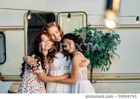 Beautiful multi ethnic girls hugging near camper van outdoors 59994743