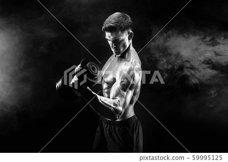 Handsome bodybuilder doing exercise with dumbbell. Studio shot. Black and white photo. Smoke 59995125