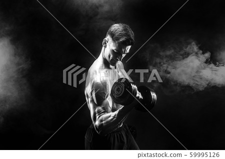 Handsome bodybuilder doing exercise with dumbbell. Studio shot. Black and white photo. Smoke 59995126
