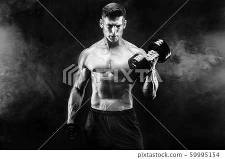 Handsome bodybuilder doing exercise with dumbbell. Studio shot. Black and white photo. Smoke Handsome bodybuilder doing exercise with dumbbell. Studio shot. Black and white photo. Smoke 59995154