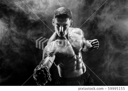 Serious muscular fighter doing the punch with the chains braided over his fist. Serious muscular fighter doing the punch with the chains braided over his fist. 59995155