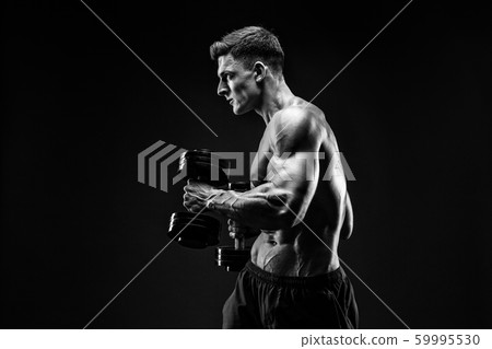 Handsome bodybuilder doing exercise with dumbbell. Studio shot. Black and white photo. 59995530
