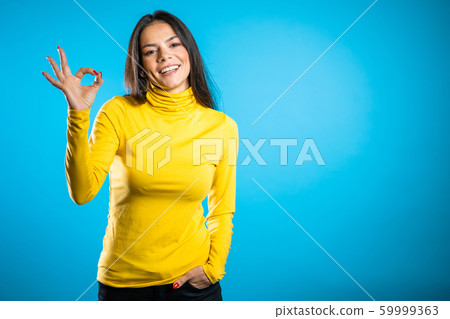 Young woman making OK sign over blue background. Winner. Success. Positive brunette young hispanic girl smiles for camera. Young woman making OK sign over blue background. Winner. Success. Positive brunette young hispanic girl smiles for camera. 59999363