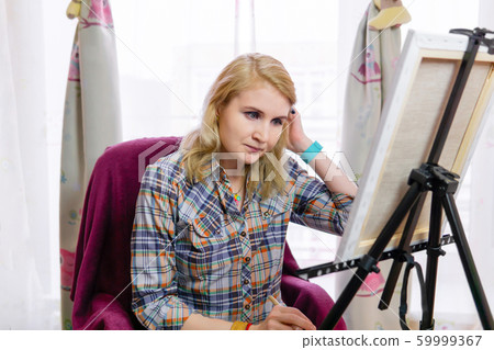 female artist looks at an easel, thinking 59999367