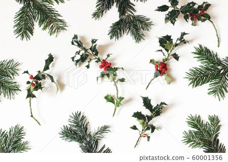 Christmas natural floral pattern. Composition of red holly berries and green fir tree branches isolated on white table background. Winter natural decoration. Botanical festive flat lay, top view. Christmas natural floral pattern. Composition of red holly berries and green fir tree branches isolated on white table background. Winter natural decoration. Botanical festive flat lay, top view. 60001356
