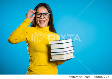 Latin student on blue background in the studio holds stack of university books from library. Guy smiles, he is happy to graduate. Copy space. Latin student on blue background in the studio holds stack of university books from library. Guy smiles, he is happy to graduate. Copy space. 60002773