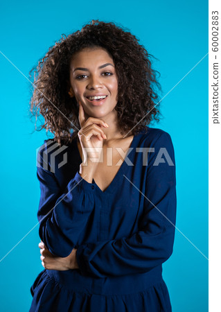 Attractive african american woman with afro hair in business clothing smiling to camera over blue wall background. Cute mixed race girl's portrait Attractive african american woman with afro hair in business clothing smiling to camera over blue wall background. Cute mixed race girl's portrait 60002883