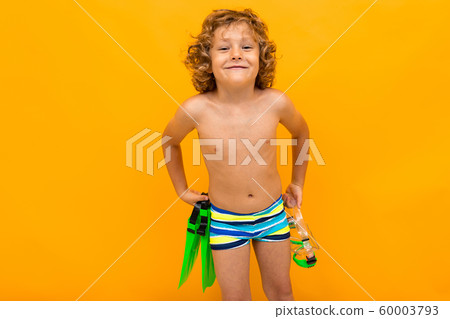 Red-haired curly boy holds swimming flippers over yellow background 60003793