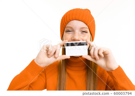 red-haired beautiful girl in an orange hat holds a credit card on an isolated white background 60003794