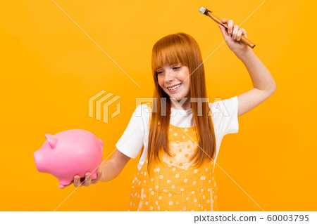 swmiling girl beats a piggy bank with a hammer on a yellow background swmiling girl beats a piggy bank with a hammer on a yellow background 60003795