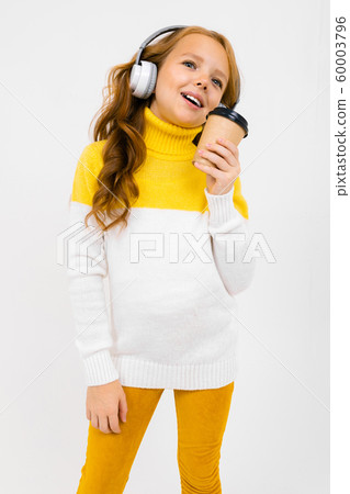 Pretty girl listens to music in big headphones and drinks coffee on a white studio background 60003796