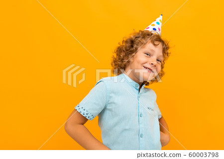 Smiling red-haired curly boy with a celebratory cap isolated yellow background Smiling red-haired curly boy with a celebratory cap isolated yellow background 60003798